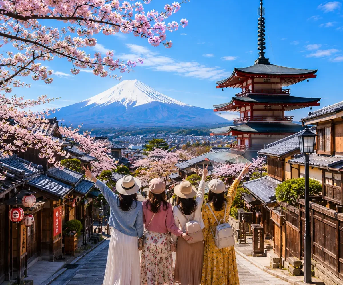 Women-only Japan tour featuring four female travellers exploring Kyoto's historic streets with the iconic Yasaka Pagoda, Mount Fuji, traditional wooden houses, and blooming cherry blossoms under a bright blue sky.