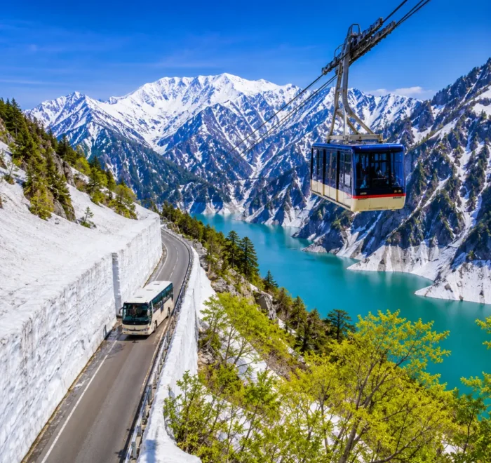 Luxury Japan Alpine Route featuring the iconic Tateyama Kurobe Snow Corridor, crystal-clear turquoise Kurobe Lake, panoramic snow-covered peaks, an alpine cable car, and a scenic mountain road under bright blue skies. No people.