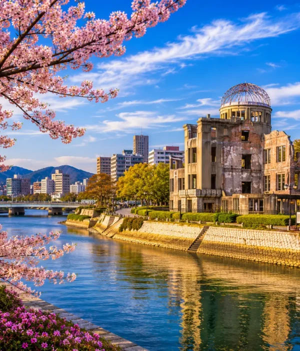 Luxury Hiroshima cityscape featuring the Hiroshima Peace Memorial (Atomic Bomb Dome), a tranquil riverside, blooming cherry blossom trees, modern skyline, and crystal-clear blue skies in bright daylight. No people.