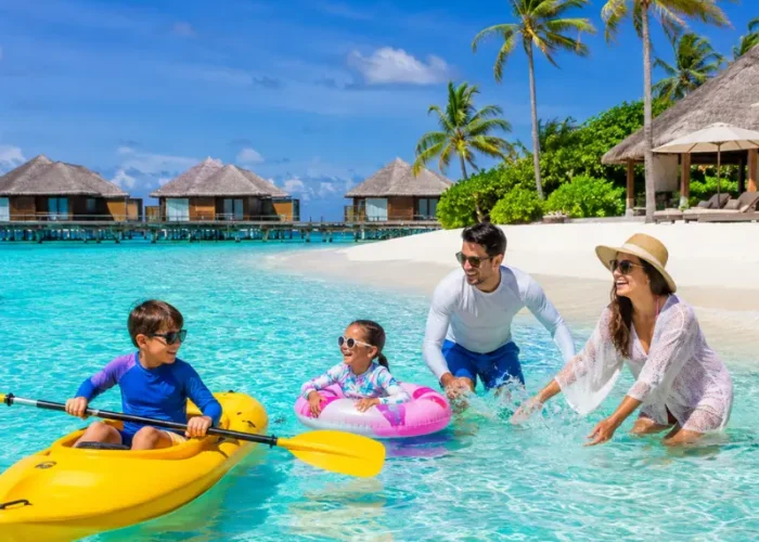 Family enjoying Maldives beach resort with turquoise lagoon, white sand, palm trees, and tropical island scenery.
