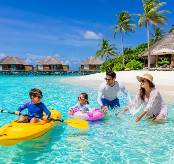 Family enjoying Maldives beach resort with turquoise lagoon, white sand, palm trees, and tropical island scenery.