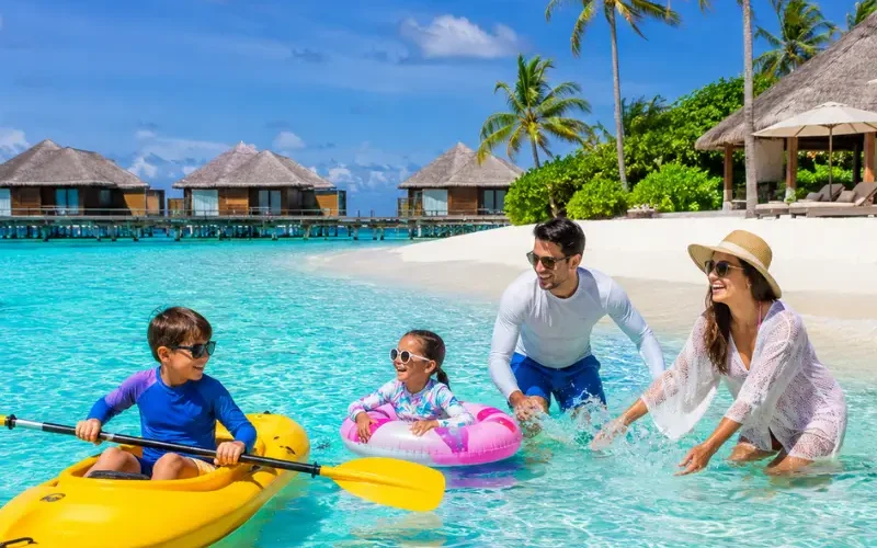 Family enjoying Maldives beach resort with turquoise lagoon, white sand, palm trees, and tropical island scenery.