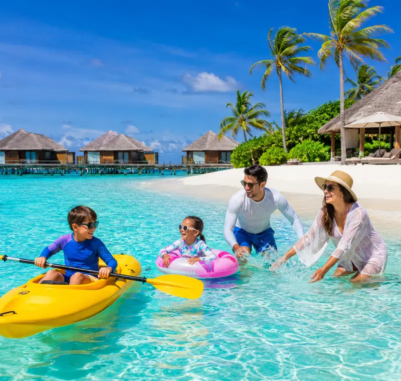 Family enjoying Maldives beach resort with turquoise lagoon, white sand, palm trees, and tropical island scenery.