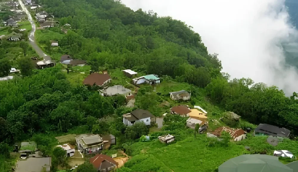 Meghalaya Explorer Package with misty hillside village, lush green forest, valley clouds and scenic Northeast India landscape