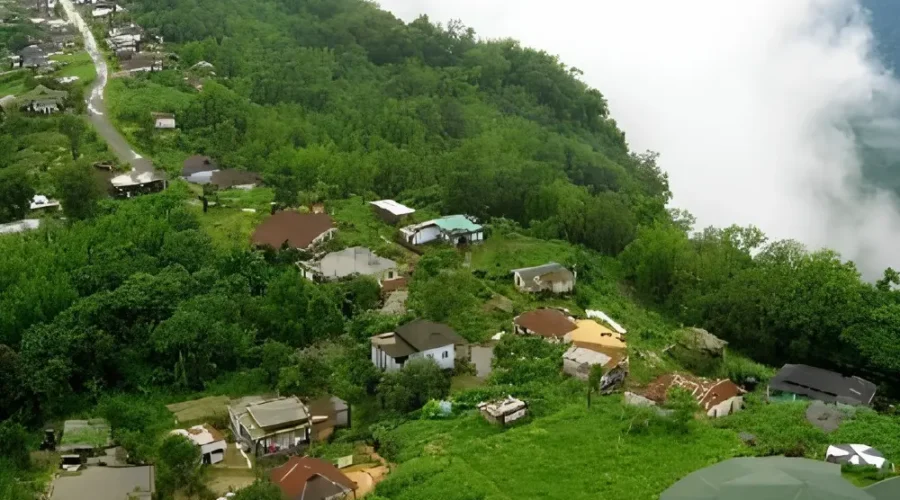 Meghalaya Explorer Package with misty hillside village, lush green forest, valley clouds and scenic Northeast India landscape