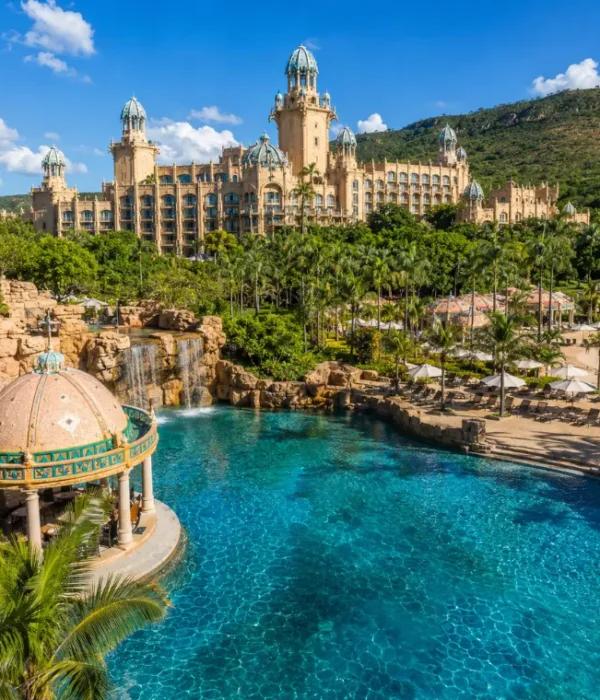 Luxury daytime view of Sun City South Africa with palace resort, turquoise pool, palm trees, and lush hills.