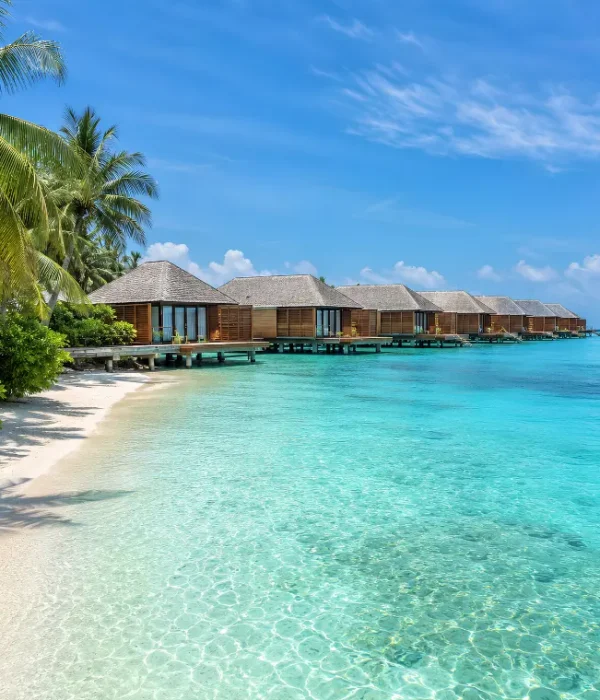 Maldives water villa resort with overwater bungalows, turquoise lagoon, white sand beach, and palm trees.