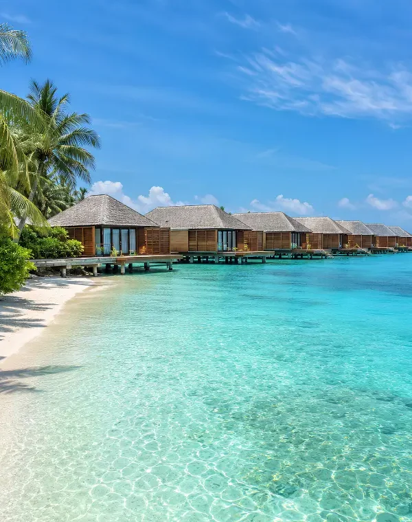 Maldives water villa resort with overwater bungalows, turquoise lagoon, white sand beach, and palm trees.