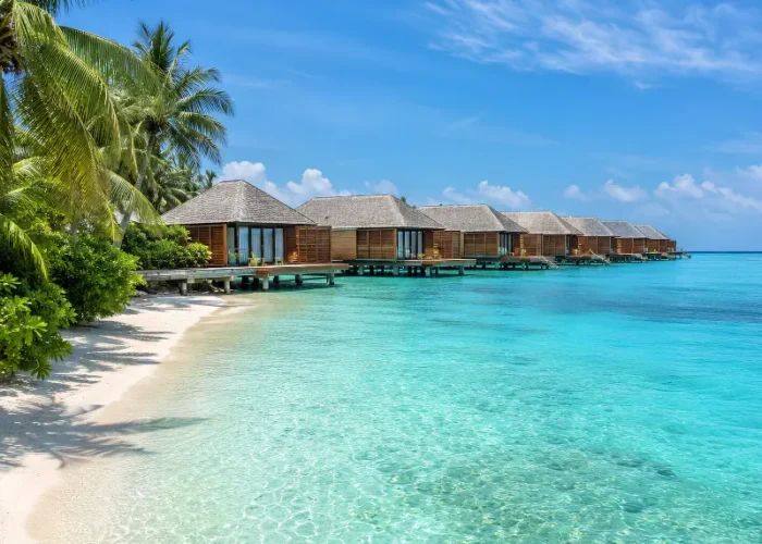 Maldives water villa resort with overwater bungalows, turquoise lagoon, white sand beach, and palm trees.