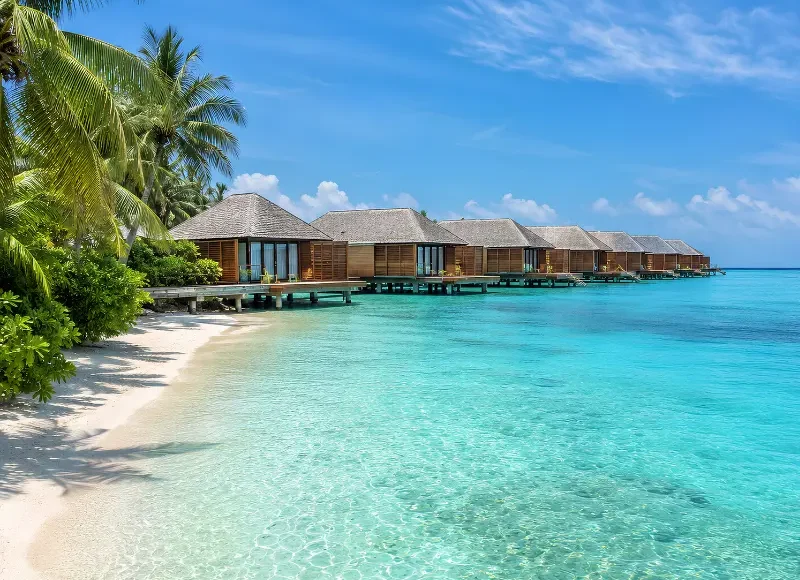 Maldives water villa resort with overwater bungalows, turquoise lagoon, white sand beach, and palm trees.