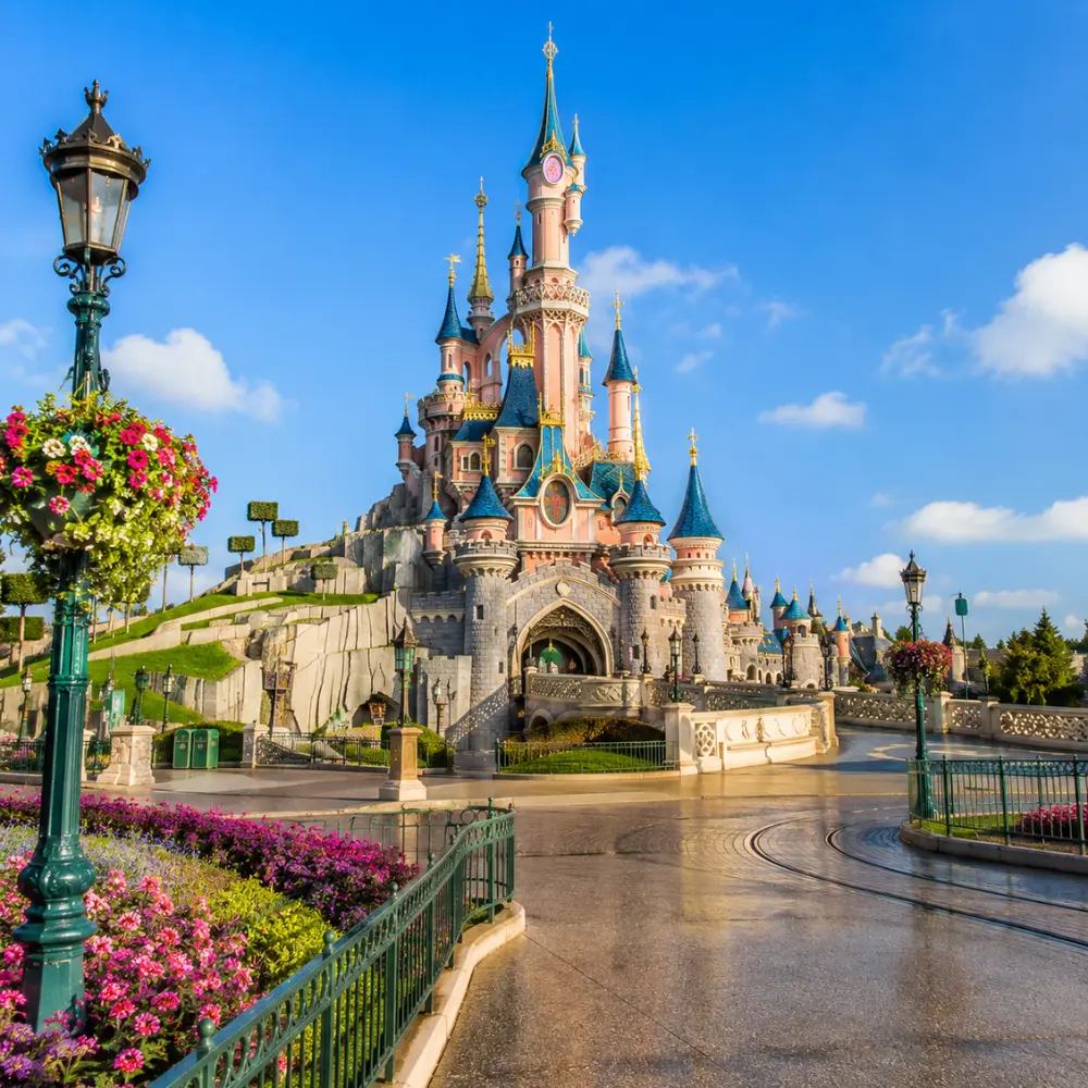 Disneyland Paris castle with fantasy gardens, clean pathways, blue sky, and bright morning family travel atmosphere