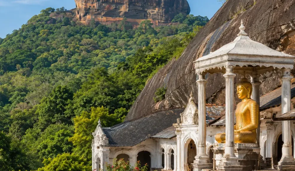 A breathtaking view of Sigiriya Rock Fortress rising dramatically above lush green forests alongside the ancient Dambulla Cave Temple with its golden Buddha statue, showcasing Sri Lanka's rich cultural heritage under a bright blue daytime sky.