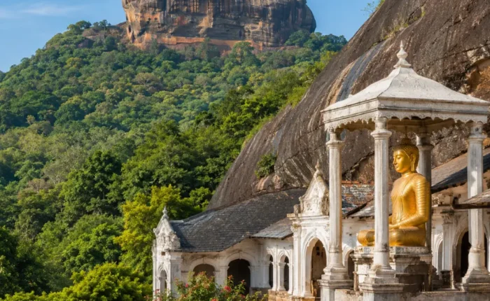 A breathtaking view of Sigiriya Rock Fortress rising dramatically above lush green forests alongside the ancient Dambulla Cave Temple with its golden Buddha statue, showcasing Sri Lanka's rich cultural heritage under a bright blue daytime sky.