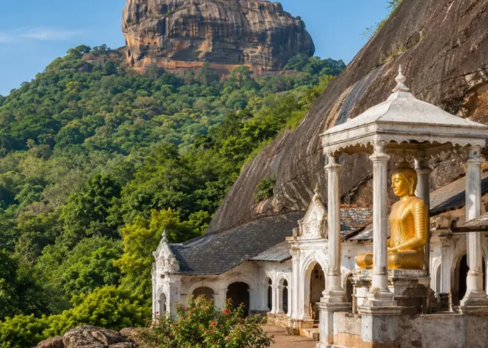 A breathtaking view of Sigiriya Rock Fortress rising dramatically above lush green forests alongside the ancient Dambulla Cave Temple with its golden Buddha statue, showcasing Sri Lanka's rich cultural heritage under a bright blue daytime sky.
