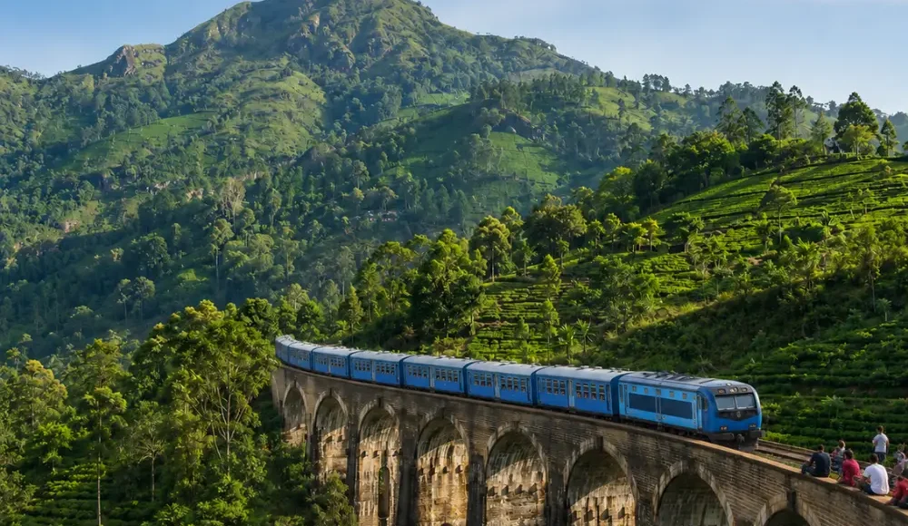 Nine Arches Bridge in Ella with a blue train, tourists enjoying the view, lush tea hills, and bright morning light.