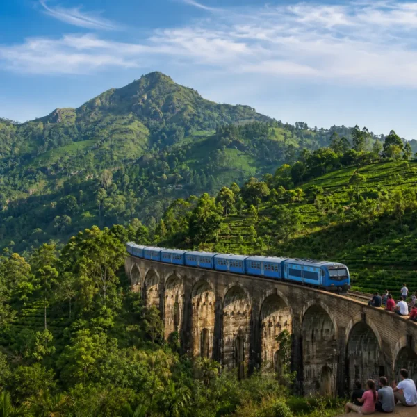 Nine Arches Bridge in Ella with a blue train, tourists enjoying the view, lush tea hills, and bright morning light.
