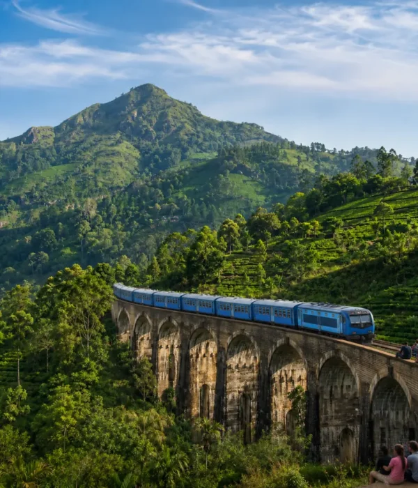 Nine Arches Bridge in Ella with a blue train, tourists enjoying the view, lush tea hills, and bright morning light.