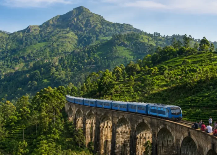 Nine Arches Bridge in Ella with a blue train, tourists enjoying the view, lush tea hills, and bright morning light.