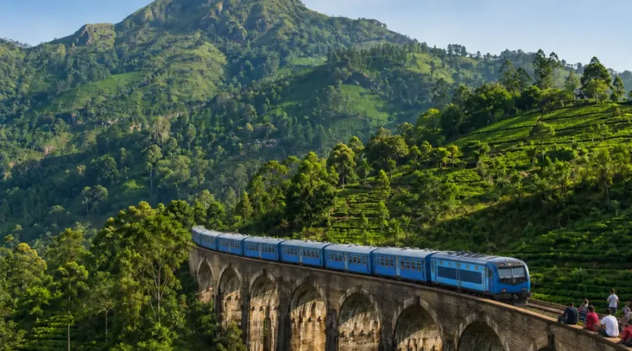 Nine Arches Bridge in Ella with a blue train, tourists enjoying the view, lush tea hills, and bright morning light.